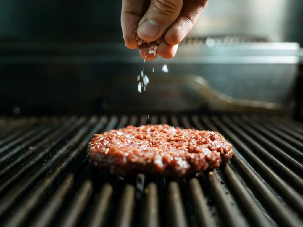 Hand's chef preparing delicious burger on grilled in the restaurant kitchen.